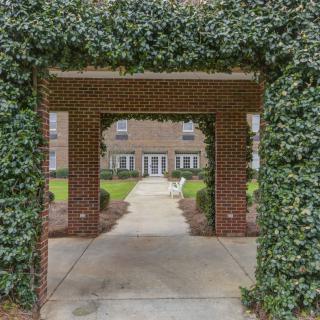 A brick archway covered in ivy leads to a pathway and a building in the background.