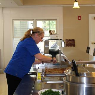 A woman in a blue uniform preparing food in a cafeteria kitchen.
