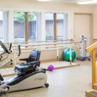 A rehabilitation room equipped with a stationary bike, parallel bars, and exercise balls for physical therapy.