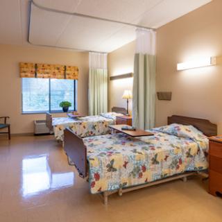 A spacious patient room in a hospital featuring two beds, warm lighting, and a view outside.