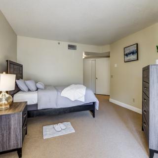 A cozy bedroom featuring a bed with pillows and a blanket, bedside table with lamp, dresser, and wall decor.