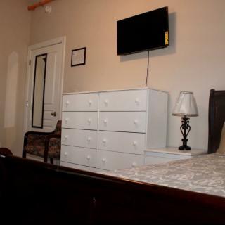 A cozy bedroom featuring a white dresser, wall-mounted TV, and a lamp on the bedside table.