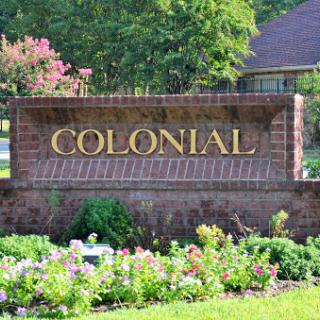 A beautifully landscaped entrance sign displaying the word 'COLONIAL' surrounded by vibrant flowers.