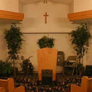 An interior view of a church with a podium, cross, and surrounding plants.