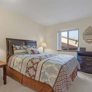 A cozy bedroom with a double bed, bedside table, lamp, and dresser near a window.