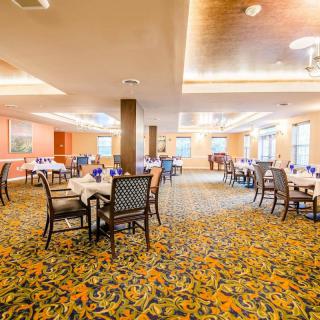 A spacious dining room with neatly arranged tables and chairs, featuring vibrant carpeting and modern lighting.