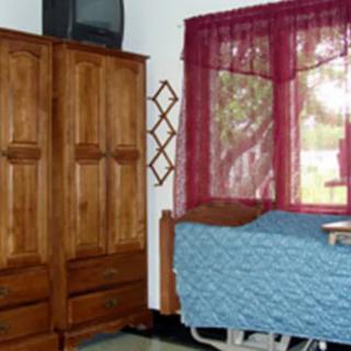 A room with a hospital bed, wooden wardrobe, and a TV next to a window with red curtains.