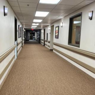 An empty, well-lit hallway with carpet flooring and framed pictures on the walls.