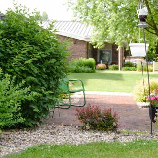 A tranquil garden with lush greenery, featuring a patio area and garden furniture.