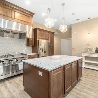 A modern kitchen featuring a central island with marble countertops, pendant lighting, wood cabinets, and stainless steel appliances.