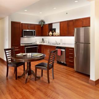 A modern kitchen with wooden cabinets, stainless steel appliances, and a small dining area featuring a round table and chairs.