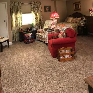 A cozy living space with a mix of a bedroom, showcasing a carpeted floor, comfortable seating, and warm lighting.