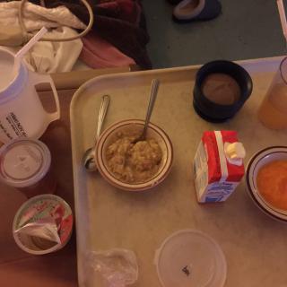 A hospital meal tray with oatmeal, a beverage, and juice.