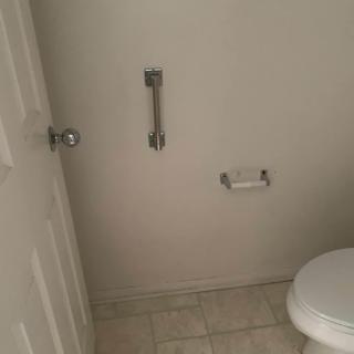 A small bathroom featuring a toilet, grab bar, and toilet paper holder.