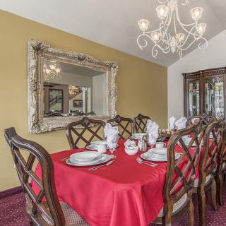 An elegantly set dining room with a red tablecloth and chandelier.