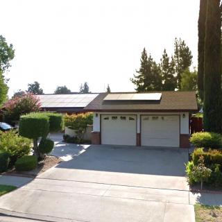 A suburban house with a driveway and solar panels on the garage roof, surrounded by well-maintained landscaping.