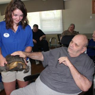 A caregiver introduces a turtle to residents in a communal space, promoting engagement and joy.
