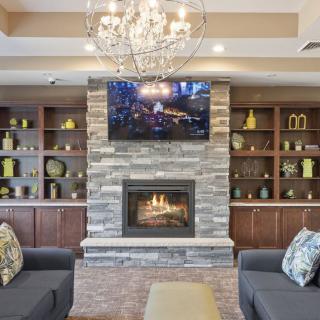A cozy living room featuring a stone fireplace, a chandelier, and a TV mounted above the mantel. The room is furnished with comfortable couches and decorative shelves.