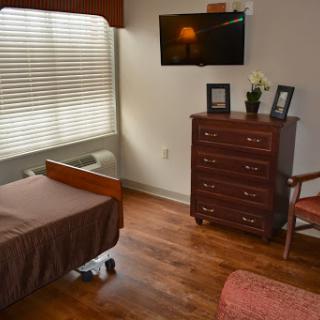 A comfortable hospital patient room featuring a bed, dresser, and television.