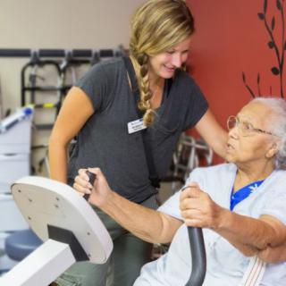 A healthcare professional assists an elderly person during a rehabilitation exercise session.