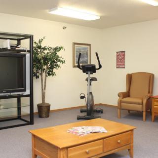 A living room with an exercise bike, TV, coffee table, and armchair arranged neatly.