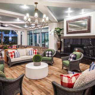 A cozy living room with comfortable seating around a fireplace, accented by plaid pillows and a chandelier.