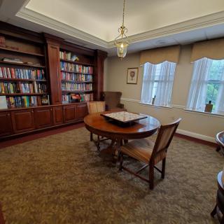 A cozy library room with bookshelves, a round table, and chairs near large windows.