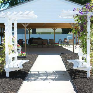 A charming pergola with benches and flowers lines a pathway leading to an outdoor seating area.
