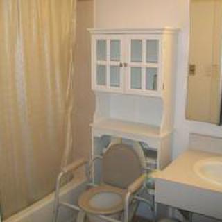 A bathroom featuring a storage cabinet, sink, shower curtain, and commode chair.