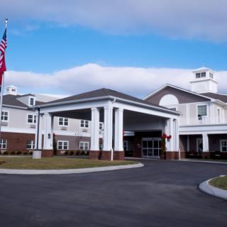 A modern hospital building with an American flag and a spacious driveway under a cloudy sky.