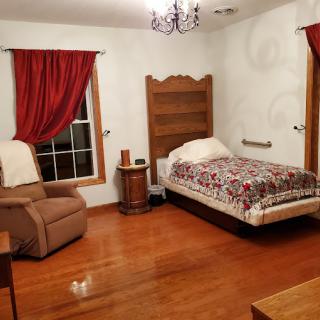 A cozy bedroom with a single bed and armchair, featuring wooden floors and red curtains.