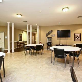A spacious and well-lit conference room with round tables and chairs, featuring a mounted television on the wall.