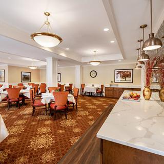 A well-lit dining area with neatly arranged tables and chairs, featuring elegant chandeliers and a patterned carpet.