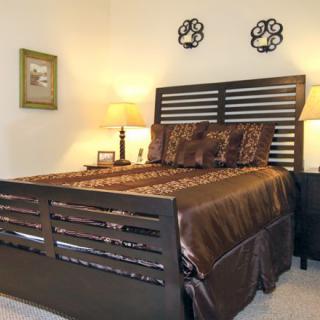 A cozy bedroom with a dark wooden bed frame, stylish bedding, and warm lighting.