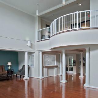 A modern living room with a high ceiling, featuring a balcony, columns, and hardwood flooring.