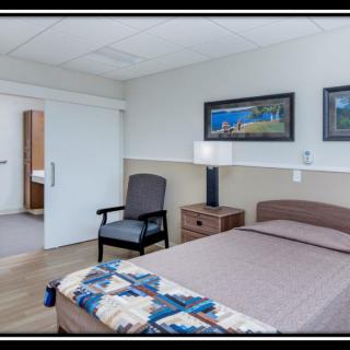 A cozy bedroom with a bed, chair, and nightstand, featuring art on the walls.