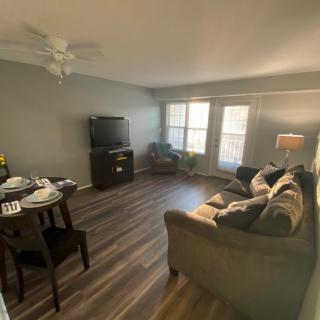A cozy living room with a sofa, television, and a small dining area illuminated by natural light.