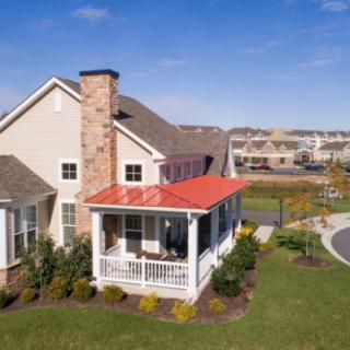 A suburban house with a red roofed porch and a well-maintained lawn under a clear blue sky.