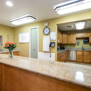 A well-lit office reception area with a counter, flowers, and a view into a small kitchen.