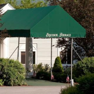 An entrance with a green awning labeled 'Grand House', surrounded by plants and landscaping.