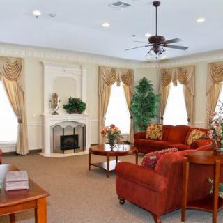 A cozy living room with elegant decor, featuring red sofas, a fireplace, and large windows with draped curtains.