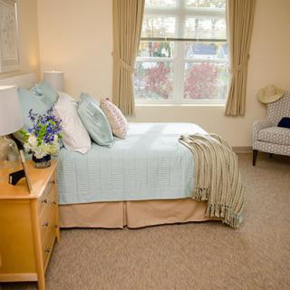 A cozy bedroom with a neatly made bed, soft decor, and a window bringing in natural light.