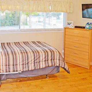 A cozy bedroom with a striped bedspread, wooden dresser, and large window.
