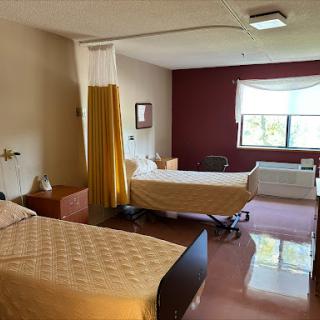 A spacious patient room in a hospital, featuring two beds and ample natural light.