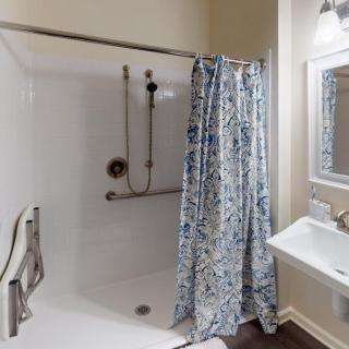 A bathroom featuring a shower with a floral curtain, grab bar, and a pedestal sink with a mirror above.