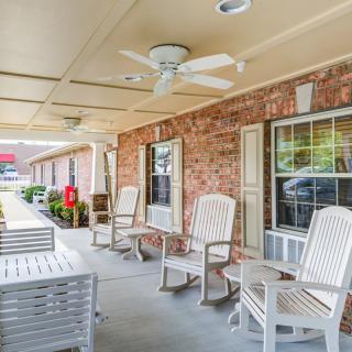 A cozy porch area with comfortable chairs and a ceiling fan under a covered patio.
