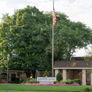A welcoming entrance featuring a flag, landscaped surroundings, and a sign.