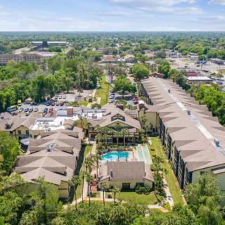Aerial view of an apartment complex with a swimming pool surrounded by trees and buildings in a suburban area.