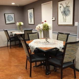 A cozy dining room with neatly arranged tables and chairs, adorned with floral decorations and framed artwork on the walls.