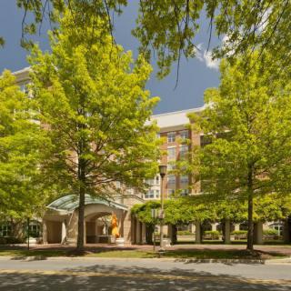 A building entrance surrounded by lush green trees under a clear blue sky.